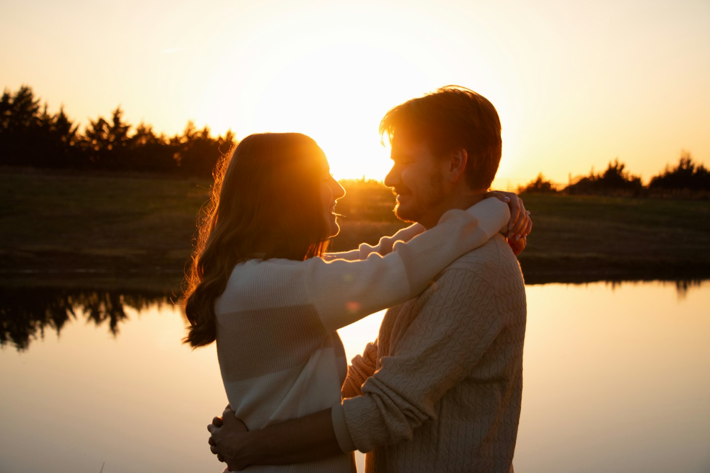 A couple embraces by a lake during a golden sunset.