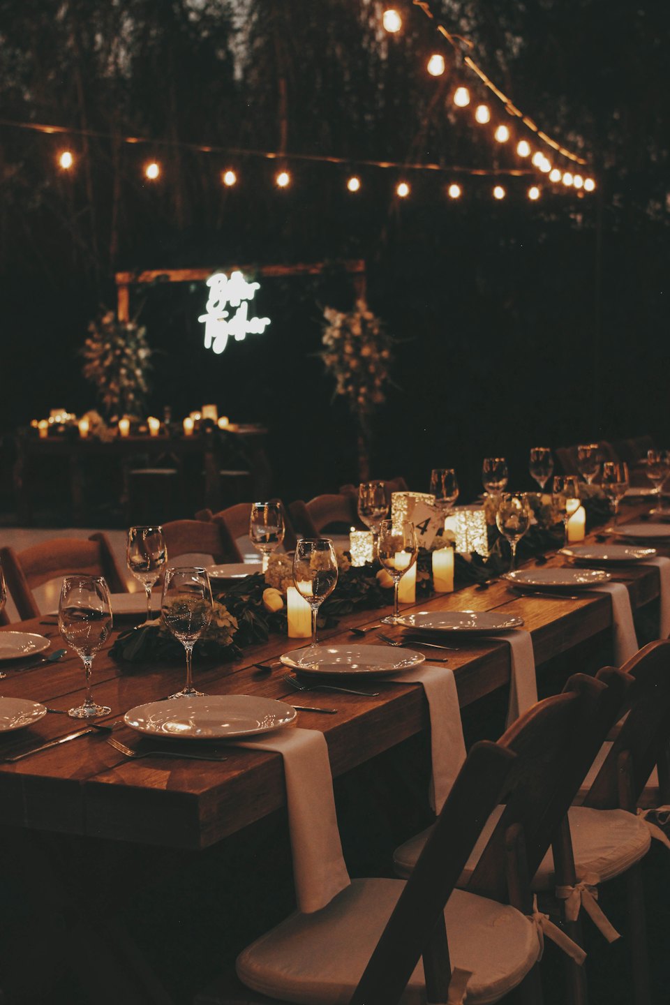 Outdoor wedding table set with candles, flowers, and string lights.